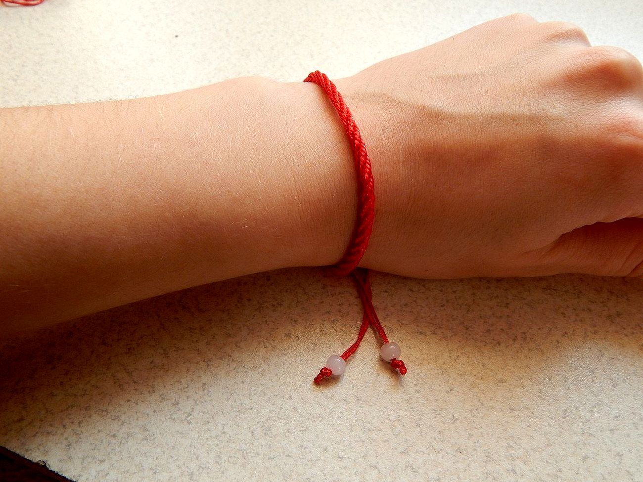 Узелок на красном браслет. Красная нитка на руке. Красная ниточка на запястье. Красные браслеты на руку.